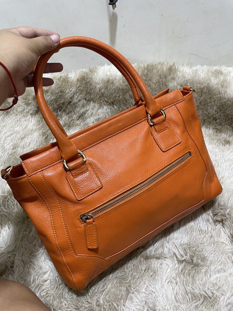 Tory Burch Orange Leather Tote Bag (Category: Shoulder Bags) located in Santiago. Submitted by UkayLuxxSelector (Listing ID 1460400747, Image 3). Description: - Stylish orange leather tote bag - Elegant gold hardware accents - Convenient front flap pocket with buckle closure - Practical zippered side pocket - Studded bottom for added protection and durability - Generously spacious interior - Ideal for everyday use and errands.