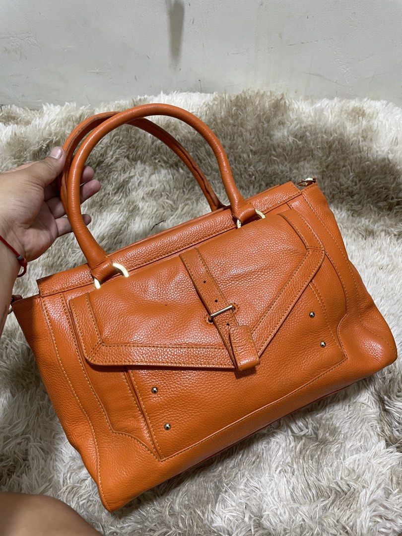 Tory Burch Orange Leather Tote Bag (Category: Shoulder Bags) located in Santiago. Submitted by UkayLuxxSelector (Listing ID 1460400747, Image 2). Description: - Stylish orange leather tote bag - Elegant gold hardware accents - Convenient front flap pocket with buckle closure - Practical zippered side pocket - Studded bottom for added protection and durability - Generously spacious interior - Ideal for everyday use and errands.