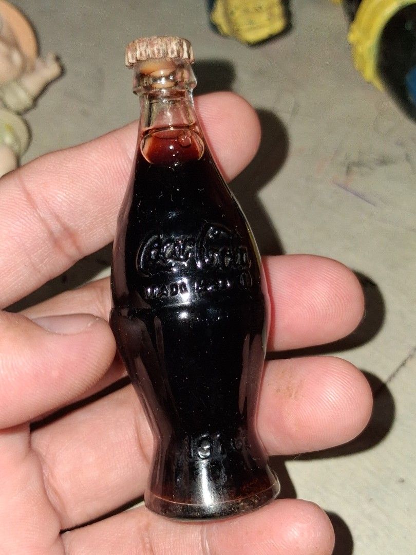 Vintage Miniature Coca-Cola Bottle with Liquid (Category: Vintage Collectibles) located in Manila. Submitted by marcas022798212 (Listing ID 1460440054, Image 1). Description: Small glass bottle shaped like a classic Coca-Cola bottle. It has the Coca-Cola logo embossed on the side. There's some dark liquid still inside. Great for collectors or as a tiny display piece. Measures about 2 inches long..