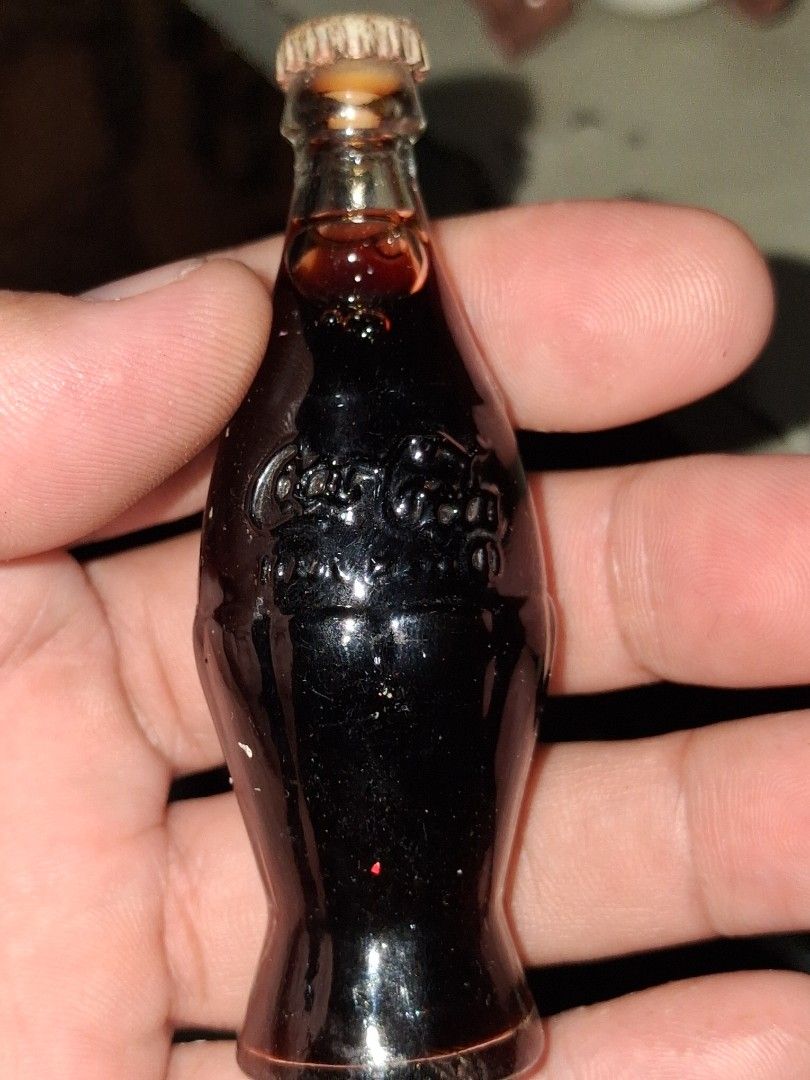 Vintage Miniature Coca-Cola Bottle with Liquid (Category: Vintage Collectibles) located in Manila. Submitted by marcas022798212 (Listing ID 1460440054, Image 2). Description: Small glass bottle shaped like a classic Coca-Cola bottle. It has the Coca-Cola logo embossed on the side. There's some dark liquid still inside. Great for collectors or as a tiny display piece. Measures about 2 inches long..
