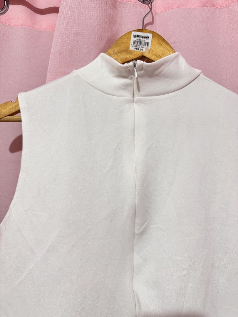 White Mock Neck Sleeveless Top (Category: Sleeveless) located in Valenzuela. Submitted by declutterlangpo (Listing ID 1460495175, Image 2). Description: - White sleeveless top - Mock neck design - Small black logo on left side - Zipper closure at the back - Ideal for layering or wearing alone - Versatile addition to your wardrobe.
