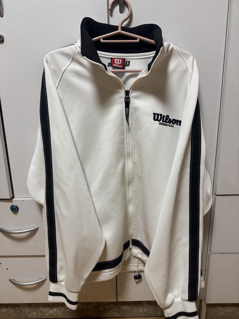 Wilson USA Track Jacket (Category: Coats, Jackets and Outerwear) located in Manila. Submitted by quintessesommerset (Listing ID 1460502434, Image 1). Description: - Classic white Wilson track jacket 23.5x27 - Black accent details - Embroidered Wilson logo and "Chicago U.S.A." on chest - Zip-up front closure - Stand-up collar - Ribbed cuffs and hem - Ideal for casual wear or sports activities.