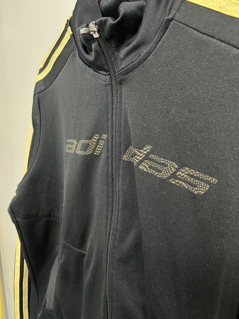 Adidas Black & Gold Full-Zip Track Jacket (Category: Coats, Jackets and Outerwear) located in Valencia. Submitted by shopstnd (Listing ID 1460698593, Image 3). Description: Adidas Black & Gold Full-Zip Track Jacket Size: L 📏 Measurements: 22 × 28 in ⭐ Condition: 9/10 🎨 Color: 9/10 *Black with metallic gold 3-stripes and Adidas detailing *Full-zip track jacket with side pockets Minimal signs of use. Please refer to photos for actual condition an