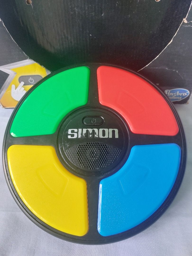 Hasbro Simon Handheld Electronic Memory Game With Lights and Sounds (Category: Educational & Learning Toys) located in Paranaque City. Submitted by ca.firstonlinebiz (Listing ID 1460687048, Image 2). Description: Preloved Classic Simon memory game by Hasbro - Features flashing lights and sounds to test your memory - Includes four colored buttons: red, blue, yellow, and green - Original box is included (shows some wear) - Fun retro electronic game