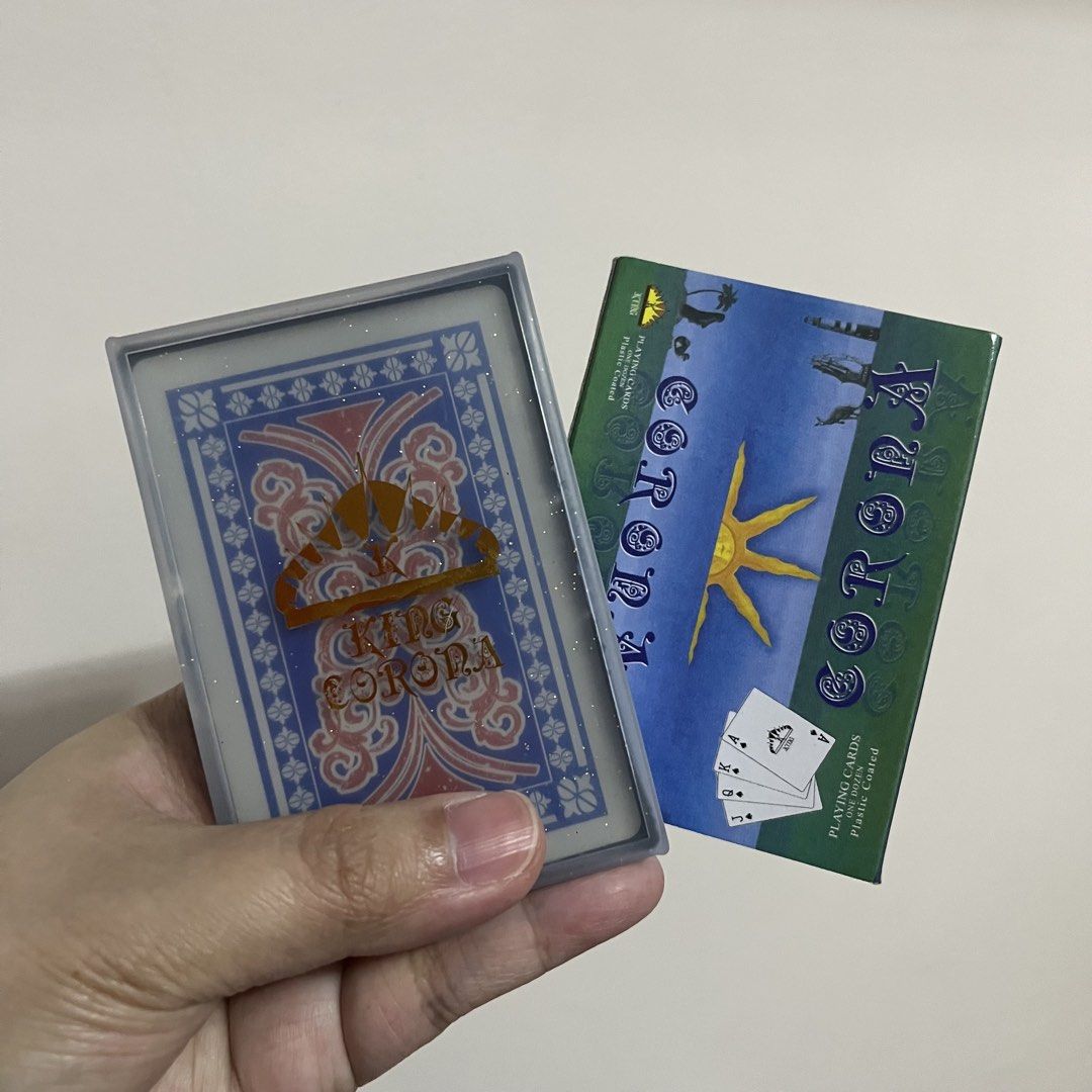 King Corona Playing Cards - Plastic Coated (Category: Board Games & Puzzles) located in San Pedro. Submitted by rainyydayy (Listing ID 1460654267, Image 1). Description: - King Corona playing cards - Plastic coated for enhanced durability - Back design: Blue and pink pattern with gold crown and 'KING CORONA' text - Box design: Blue and green with a sun graphic - Ideal for magic tricks and card games.