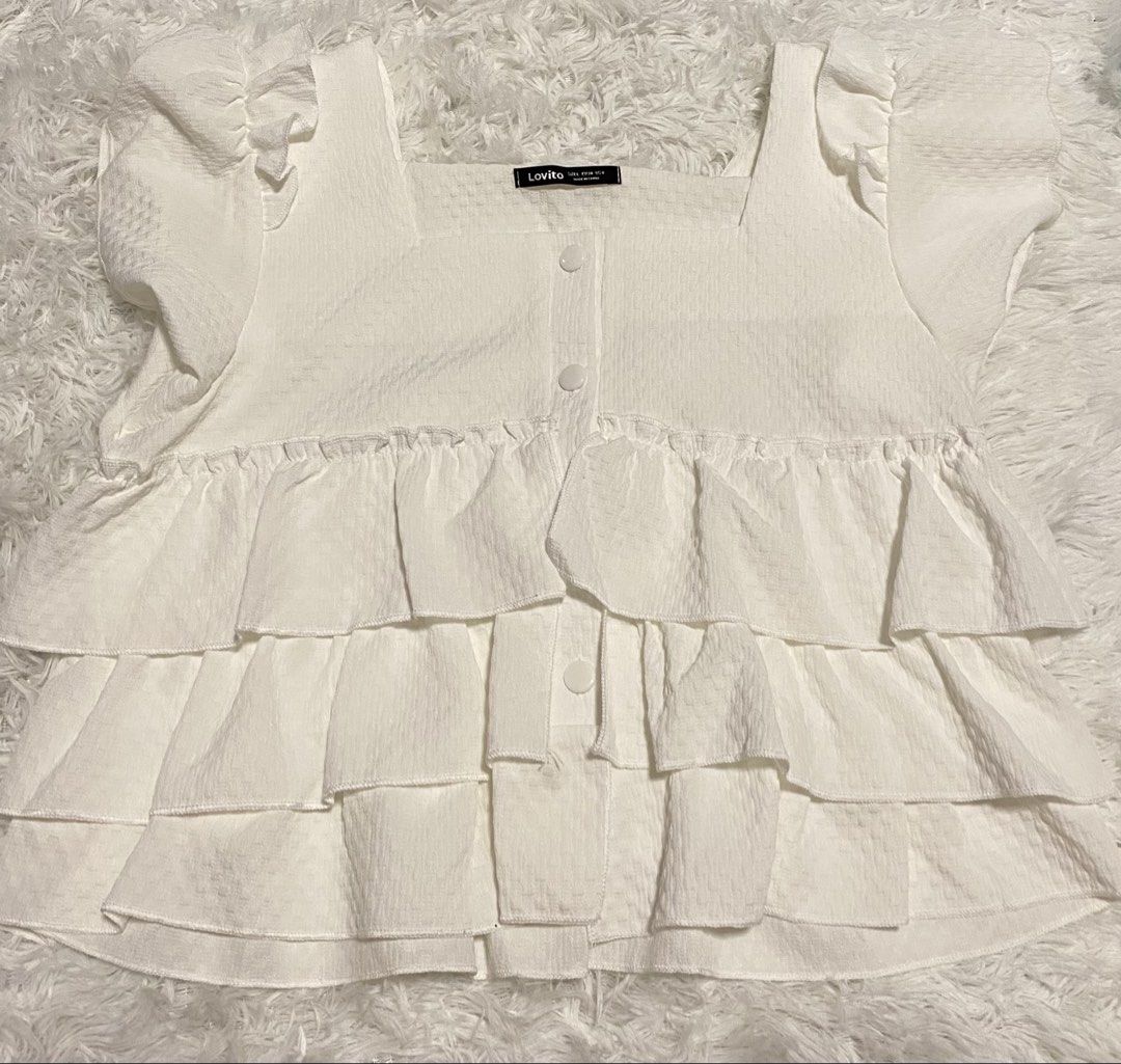 Lovito White Ruffled Square Neck Top (Category: Blouses) located in Pasig City. Submitted by jnnnngg (Listing ID 1460680056, Image 1). Description: - White ruffled top from Lovito - Square neckline - Short puff sleeves - Multiple tiers of ruffles - Button-up front - Textured fabric - Perfect for casual or dressy occasions.
