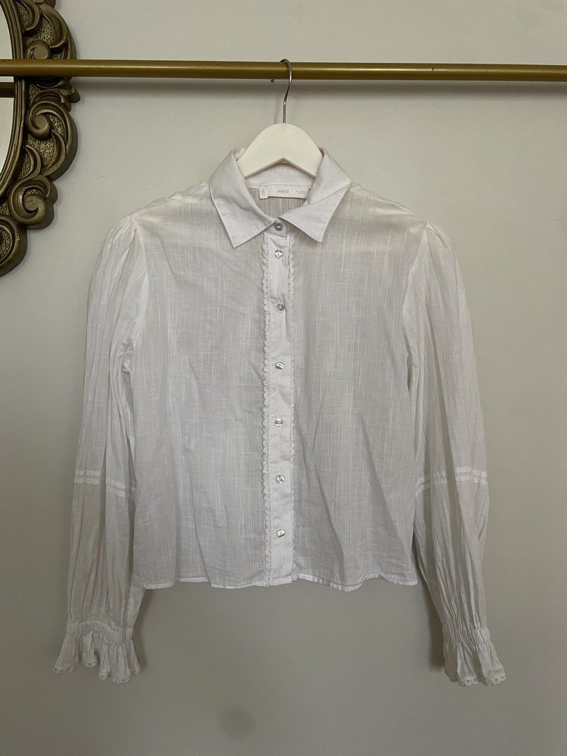 Mango White Lace Detail Button Up Blouse (Category: Blouses) located in Makati City. Submitted by alyslittlelamb (Listing ID 1460673772, Image 1). Description: - White MNG blouse - Features delicate lace trim along the buttons - Puff sleeves with ruffled cuffs - Made from a lightweight fabric - Versatile for dressing up or down - Easily pairs with jeans or skirts.