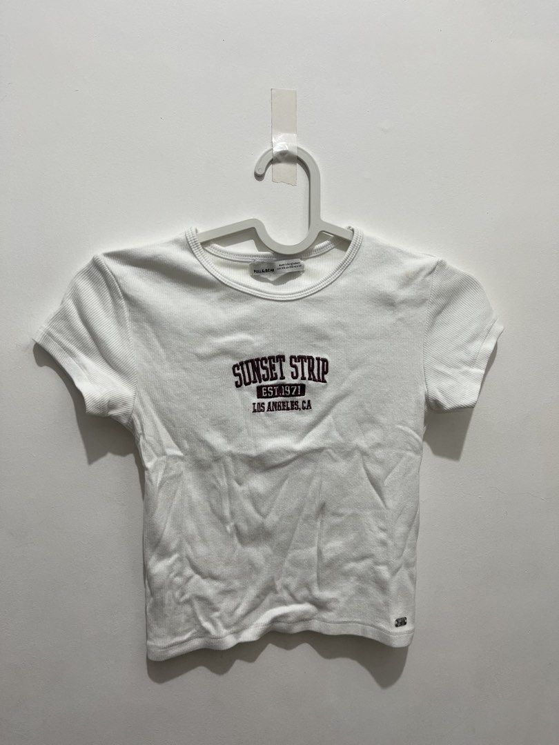 Pull & Bear White Ribbed Crop Top Sunset Strip LA (Category: Shirts) located in Manila. Submitted by jonalainea95245 (Listing ID 1460708095, Image 1). Description: - Brand: Pull & Bear - Style: White ribbed crop top - Graphic: 'Sunset Strip Est 1971 Los Angeles, CA' - Features: Short sleeves, crew neck - Condition: Small stain on the right shoulder area (please check photos for details) RFS: decluttering Location: Malabon.
